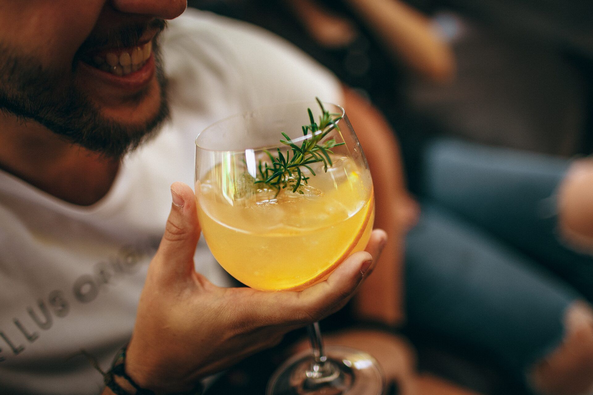 Hand hält einen Cocktail mit Rosmarin